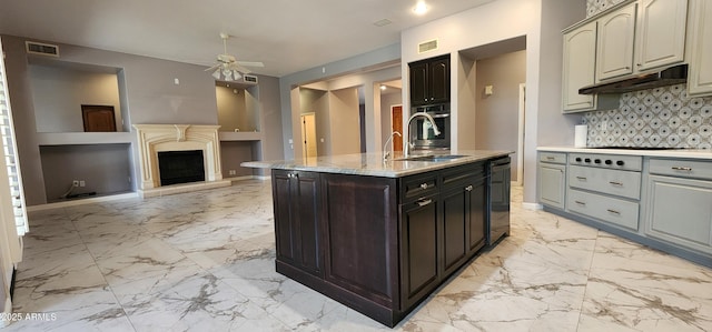 kitchen with under cabinet range hood, a sink, visible vents, marble finish floor, and a center island with sink