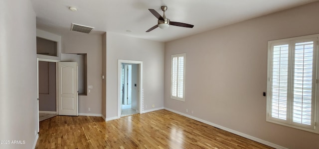 spare room with baseboards, light wood finished floors, visible vents, and a healthy amount of sunlight