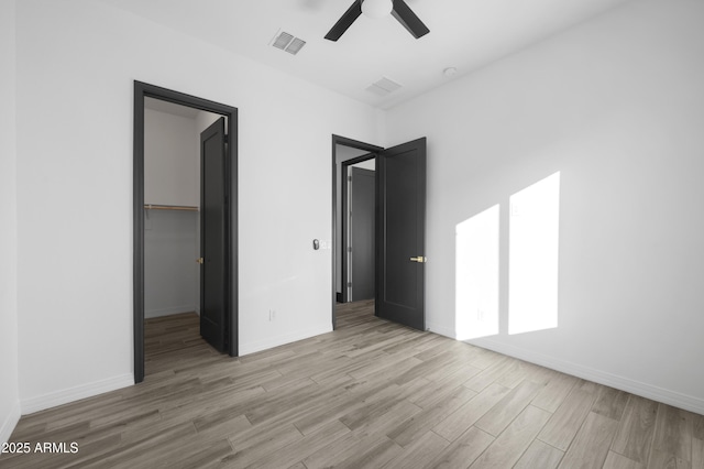 unfurnished bedroom with wood finished floors, visible vents, baseboards, a spacious closet, and a closet