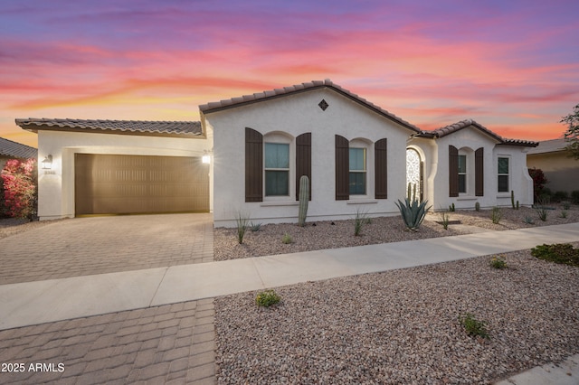 mediterranean / spanish-style house with decorative driveway, a tiled roof, an attached garage, and stucco siding