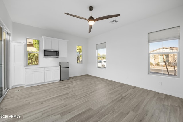 unfurnished living room with a ceiling fan, a healthy amount of sunlight, visible vents, and light wood-type flooring