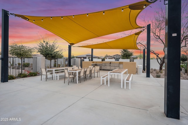 patio terrace at dusk featuring outdoor dining space and fence