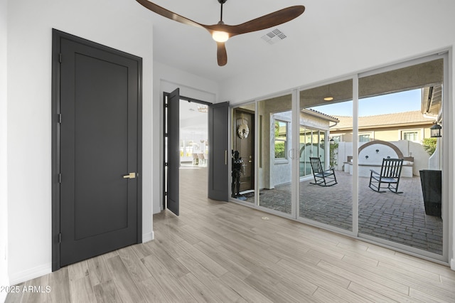 empty room with visible vents, a ceiling fan, wood finished floors, a sunroom, and baseboards