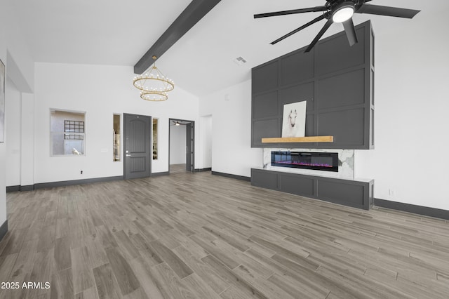 unfurnished living room featuring baseboards, visible vents, light wood finished floors, beam ceiling, and a glass covered fireplace