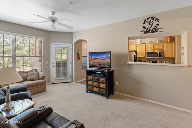 living area featuring a ceiling fan, arched walkways, light colored carpet, and baseboards