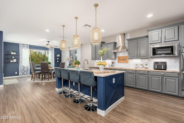 kitchen featuring gray cabinetry, light countertops, light wood-style floors, stainless steel microwave, and wall chimney exhaust hood