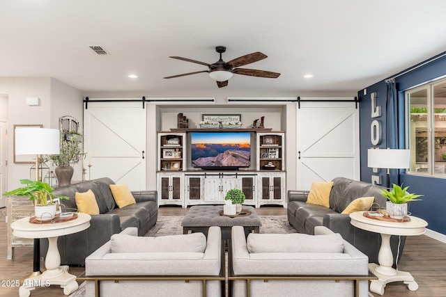 living area with a ceiling fan, a barn door, wood finished floors, and visible vents