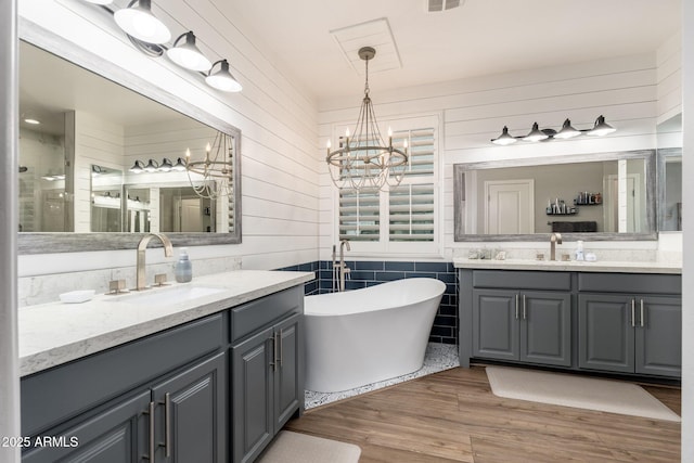 bathroom featuring a freestanding tub, wood finished floors, two vanities, and a sink