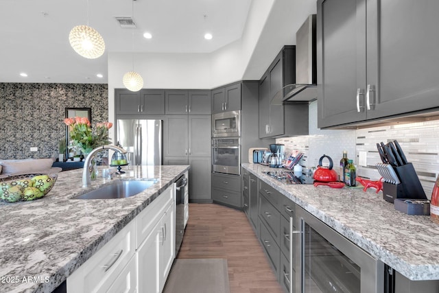 kitchen featuring gray cabinets, visible vents, appliances with stainless steel finishes, a sink, and wall chimney range hood