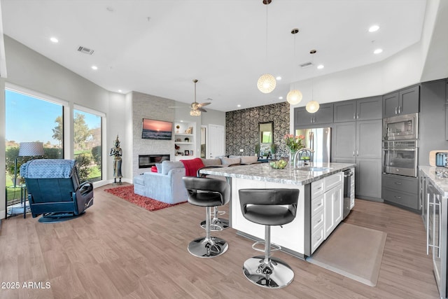 kitchen featuring a large fireplace, light wood finished floors, visible vents, open floor plan, and stainless steel appliances