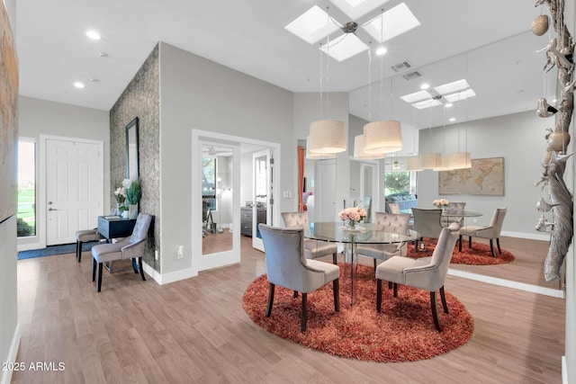 dining room with a skylight, baseboards, visible vents, a high ceiling, and light wood-type flooring