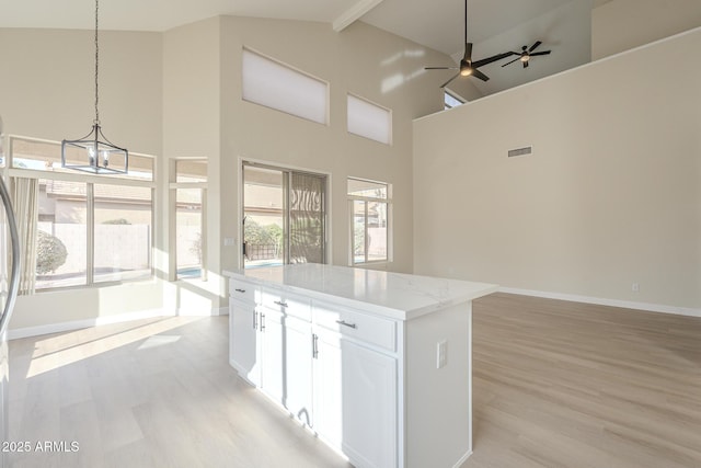 kitchen featuring a center island, white cabinets, hanging light fixtures, plenty of natural light, and light stone counters