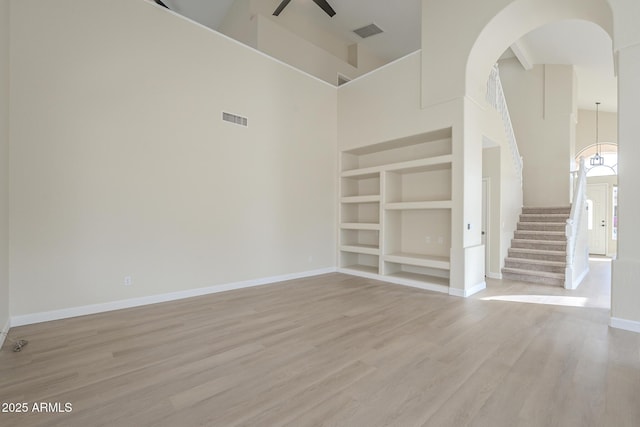 unfurnished room featuring ceiling fan, light wood-type flooring, built in features, and a high ceiling