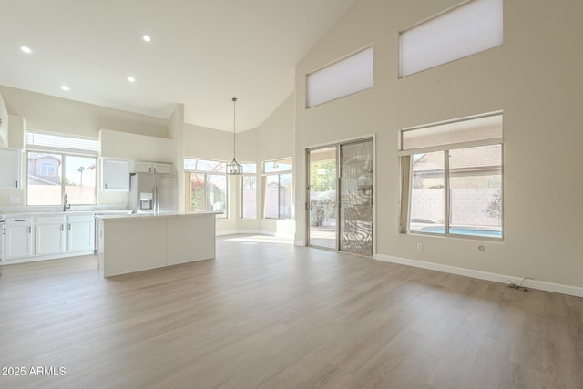 unfurnished living room featuring sink, high vaulted ceiling, a chandelier, and light wood-type flooring