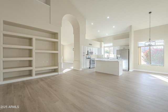 unfurnished living room featuring built in shelves, sink, a high ceiling, a chandelier, and light wood-type flooring