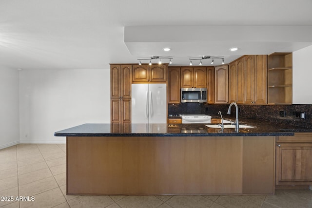 kitchen featuring sink, tasteful backsplash, dark stone countertops, kitchen peninsula, and white appliances