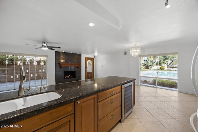 kitchen with sink, light tile patterned floors, dark stone countertops, hanging light fixtures, and beverage cooler