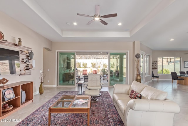 tiled living room with ceiling fan and a tray ceiling