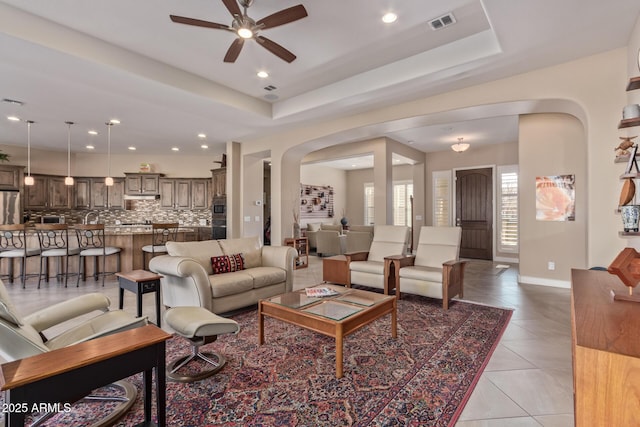 tiled living room with ceiling fan and a raised ceiling