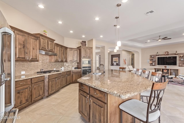 kitchen with a breakfast bar, sink, hanging light fixtures, built in appliances, and a center island with sink