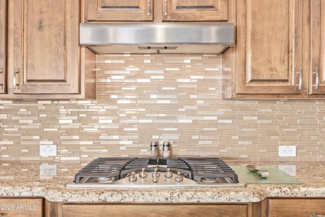 kitchen with light stone counters, decorative backsplash, and stainless steel gas stovetop