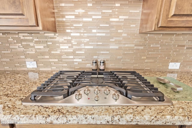 interior details with gas stovetop, light stone counters, and decorative backsplash