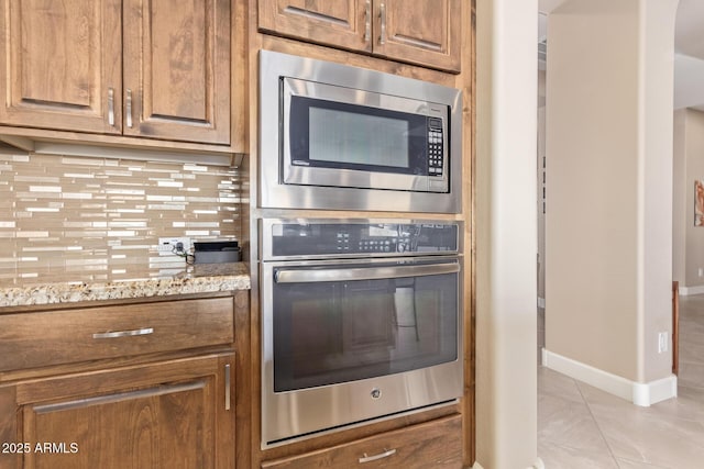 kitchen featuring appliances with stainless steel finishes, light stone countertops, light tile patterned floors, and backsplash