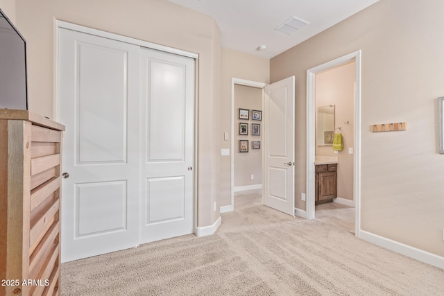 unfurnished bedroom with ensuite bathroom, light carpet, and a closet