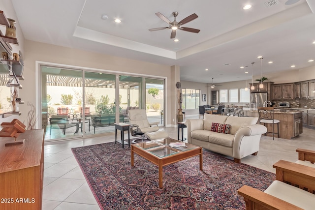 tiled living room with a raised ceiling and ceiling fan