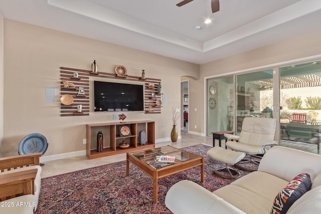 living room featuring a raised ceiling, ceiling fan, and light tile patterned flooring