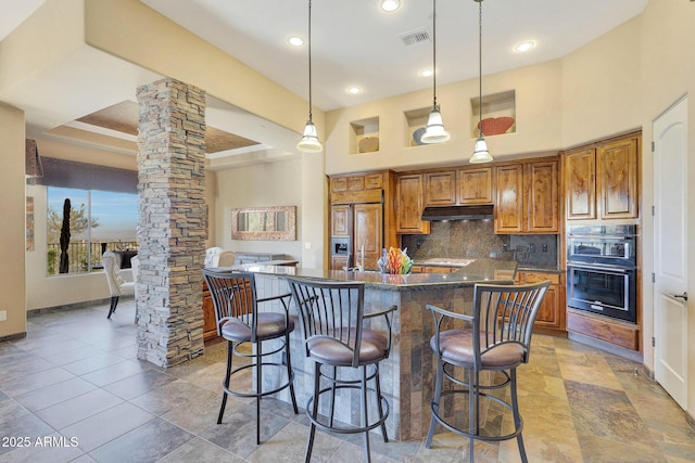 kitchen featuring ornate columns, paneled refrigerator, double oven, decorative light fixtures, and decorative backsplash