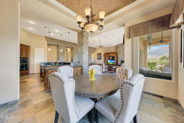 dining space featuring decorative columns, a raised ceiling, crown molding, sink, and a fireplace