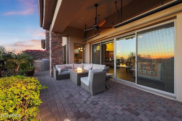 patio terrace at dusk featuring ceiling fan and an outdoor living space with a fire pit