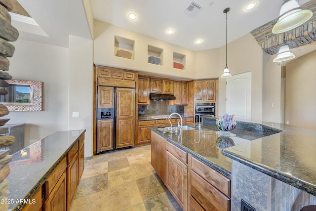 kitchen with paneled built in fridge, sink, dark stone countertops, tasteful backsplash, and decorative light fixtures