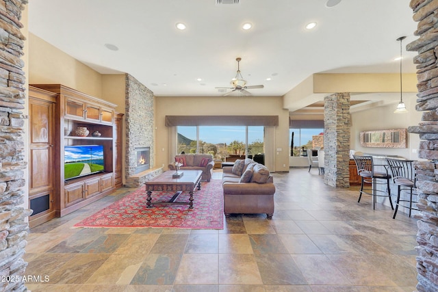 living room with a stone fireplace, ceiling fan, and ornate columns