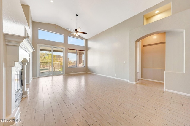 10253 E Indigo Dr, Scottsdale, AZ 85255 - unfurnished living room featuring ceiling fan, a glass covered fireplace, arched walkways, baseboards, and high vaulted ceiling
