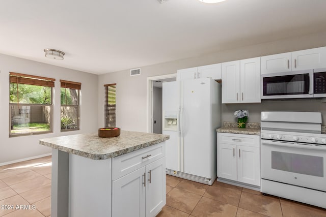 kitchen featuring white appliances, a center island, light tile patterned floors, and white cabinets