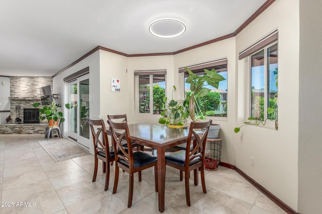 dining area featuring plenty of natural light, crown molding, a large fireplace, and baseboards