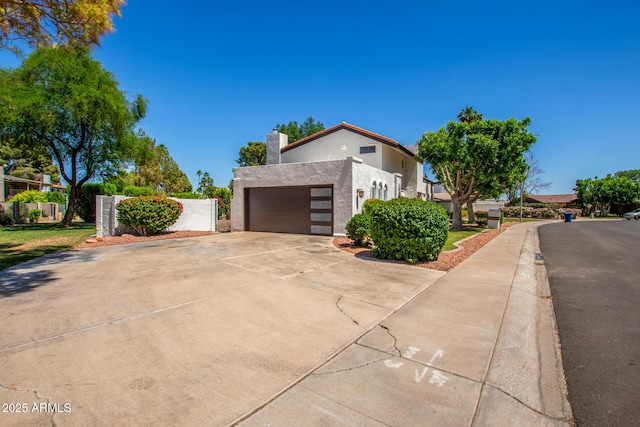 view of home's exterior with stucco siding, a garage, fence, a chimney, and driveway