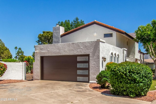 view of side of property with a garage, driveway, stucco siding, a gate, and a chimney