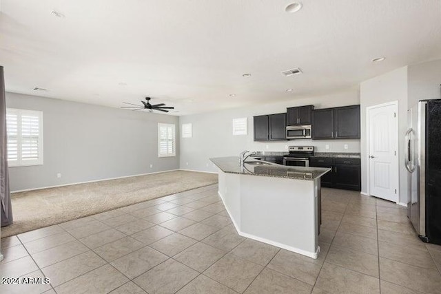 kitchen with appliances with stainless steel finishes, an island with sink, ceiling fan, light tile patterned flooring, and sink