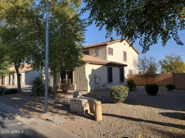 mediterranean / spanish-style home featuring a tiled roof, fence, and stucco siding