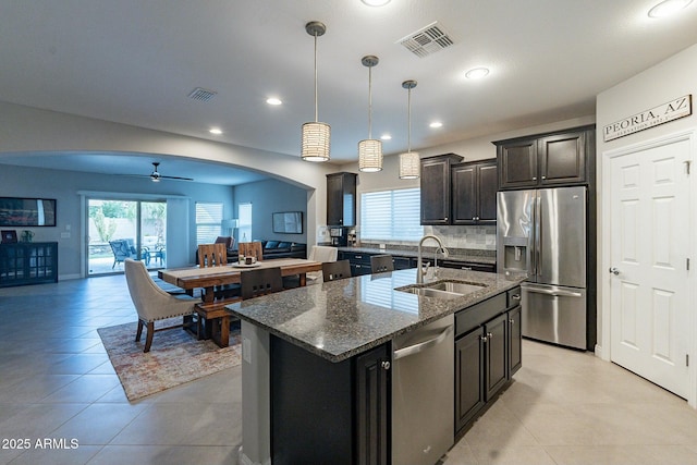 kitchen featuring sink, a kitchen island with sink, dark stone countertops, stainless steel appliances, and decorative light fixtures