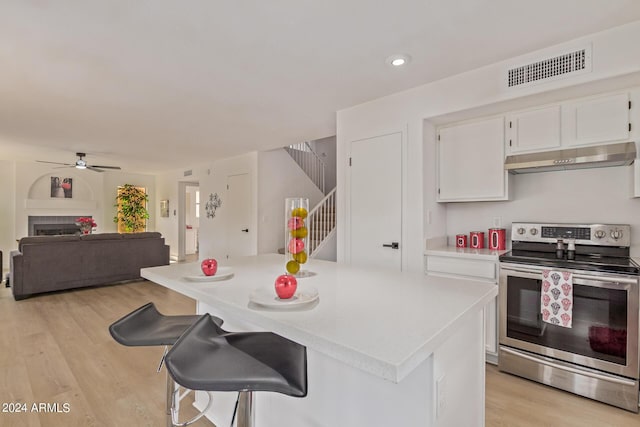 kitchen featuring a center island, a kitchen bar, white cabinetry, light wood-type flooring, and stainless steel electric range