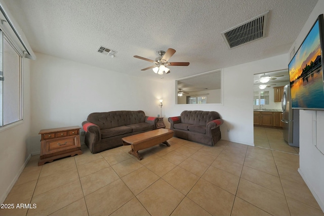 living room with light tile patterned floors, visible vents, a textured ceiling, and a ceiling fan