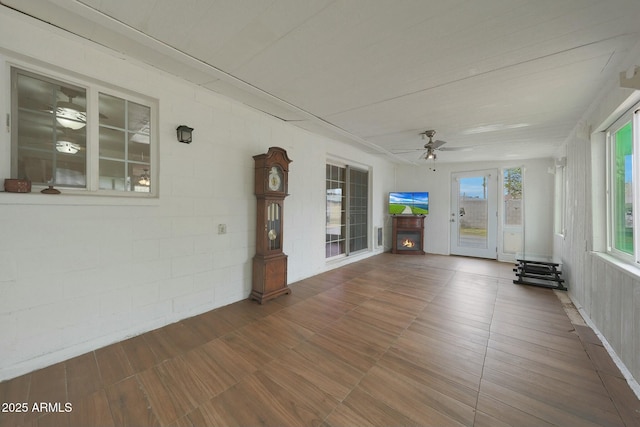 unfurnished sunroom featuring a lit fireplace and ceiling fan