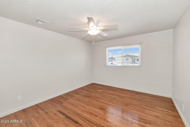 empty room featuring hardwood / wood-style floors, ceiling fan, a textured ceiling, and brick wall