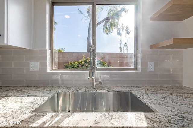 kitchen featuring light stone countertops, decorative backsplash, and sink