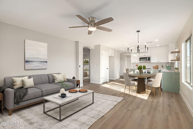 living room featuring ceiling fan with notable chandelier and light hardwood / wood-style flooring