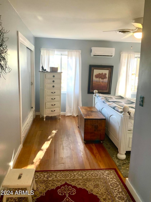 bedroom with wood-type flooring, a wall mounted AC, and ceiling fan